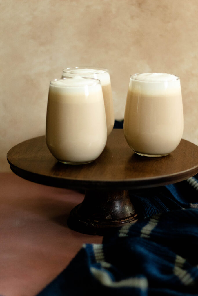 three clear glasses with harry potter butterbeer inside on a wooden cakestand.