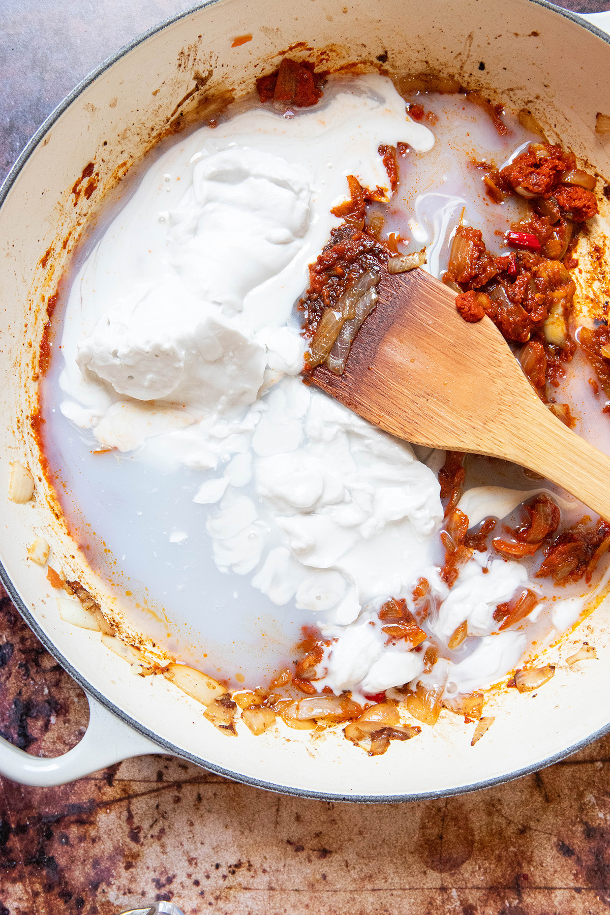 coconut milk and red curry paste in a pan with a wooden spoon