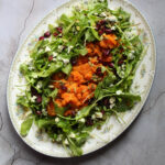 Orange butternut squash sits upon a bed of arugula with pumpkin seeds, blue cheese, and craisins.
