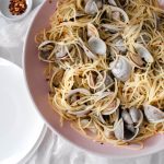 Linguine and clams with red pepper flakes sitting in a pink serving bowl.