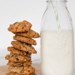 Cookies stacked in a pile next to a glass container with milk.
