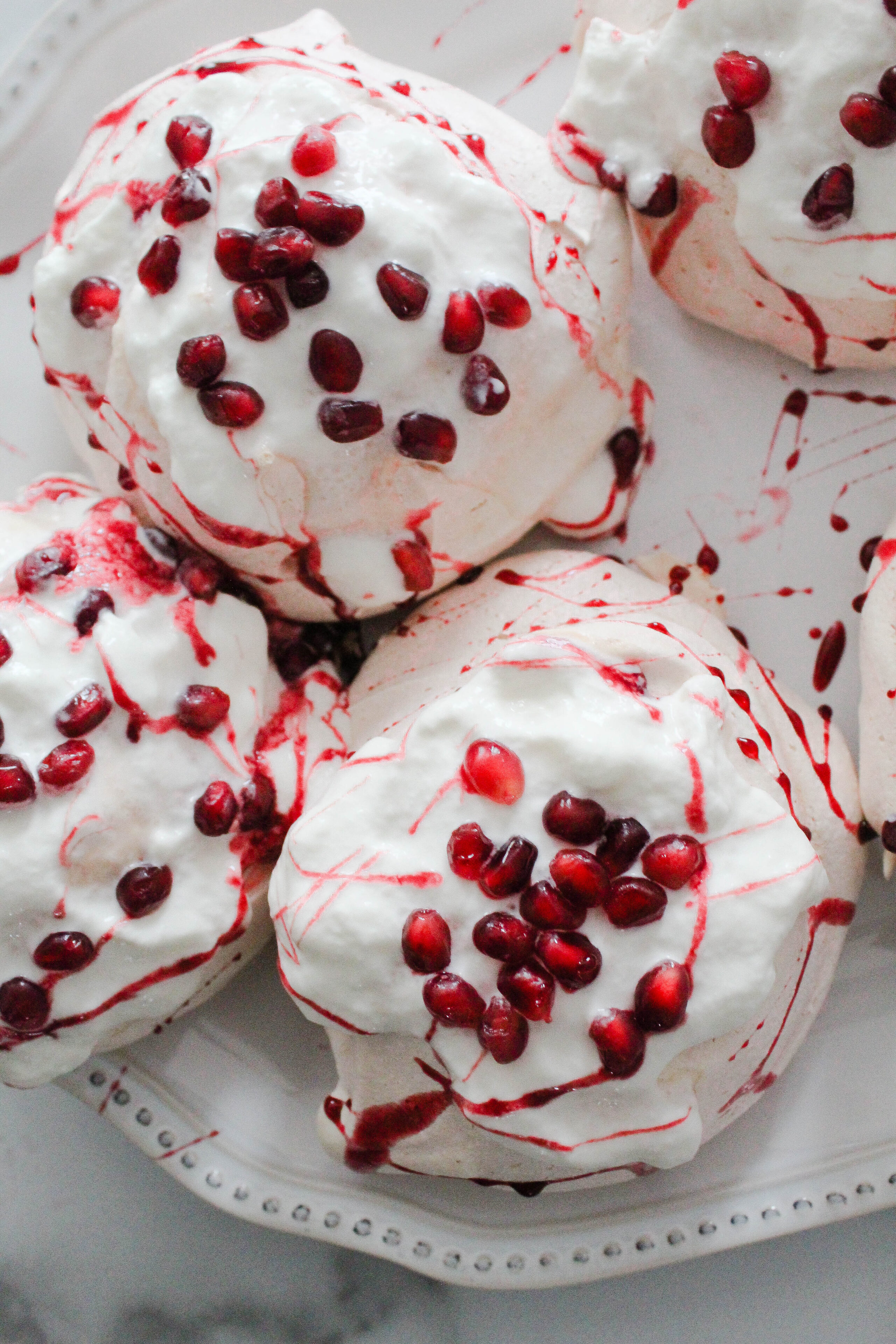 Pomegranate mini pavlovas on a white tray covered in whipped cream and pomegranate syrup and seeds.