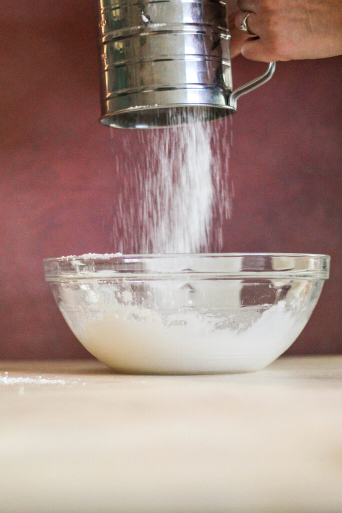 sugar being sifted into a bowl
