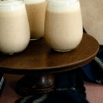 three clear glasses with harry potter butterbeer inside on a wooden cakestand.