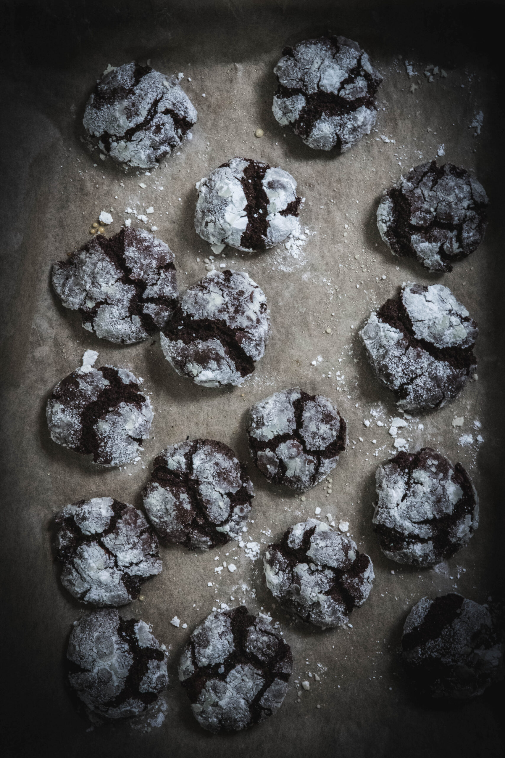 Easy Gluten Free Chocolate Crinkle Cookies laying flat on a cookie tray on brown parchment paper