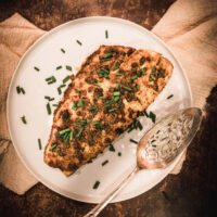 baked rockfish with chives on top on a white plate with a silver serving utensil next to it